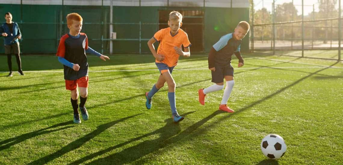 3 Kinder spielen Fußball und laufen dem Ball hinterher.