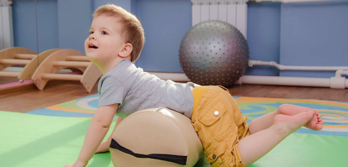 Ein Kind liegt mit dem Bauch auf einer Rolle und macht Gymnastik.