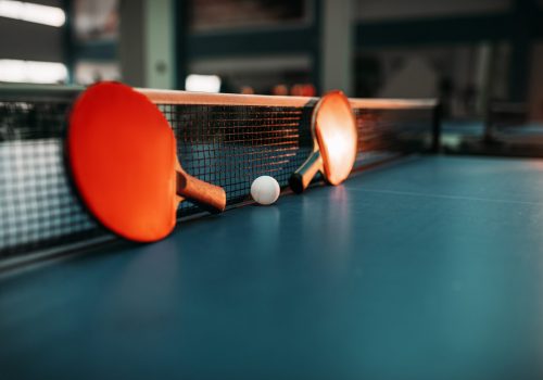 2 Tischtennisschläger und ein Tischtennisball liegen auf einer Tischtennisplatte.